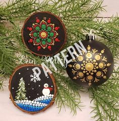 three painted christmas ornaments sitting on top of a wooden tree slice next to evergreen branches