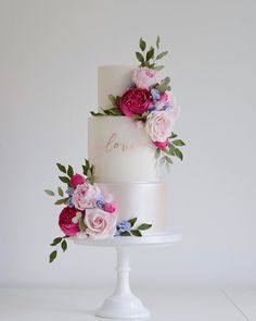 a three tiered white cake with pink and blue flowers on it's side