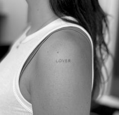 a woman with a tattoo on her shoulder that says lover in cursive writing