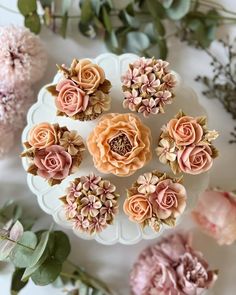 some pink flowers are sitting on a white plate next to green leaves and dried flowers