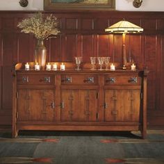 a buffet table with candles and vases on it in front of a wooden paneled wall