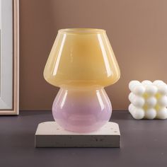 a yellow and pink lamp sitting on top of a table next to a white vase