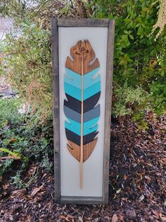 a wooden sign with a blue and black feather on it in front of some bushes