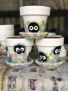 four cups with faces painted on them sitting on top of a newsprinted table