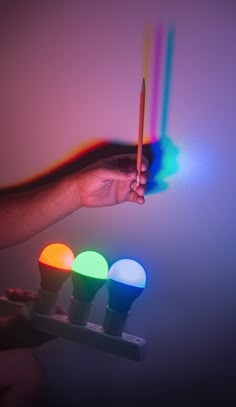 a person is holding three different colored lights in one hand and pointing to the light on the other