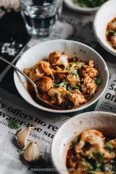 three bowls of food on top of a newspaper next to some glasses and spoons