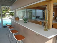 an outdoor bar with several chairs next to it and a swimming pool in the background