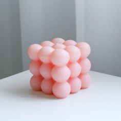 a pink candle that is sitting on a table with white walls in the back ground