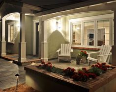 the front porch is lit up at night with red flowers and potted plants in the foreground