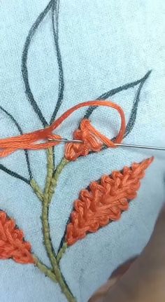 an orange flower is being stitched on to a white piece of fabric with scissors