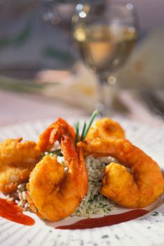 a plate with shrimp and rice on it next to a glass of wine