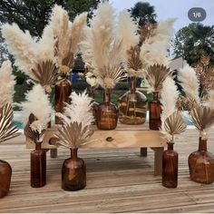 several brown vases with white flowers and feathers in them sitting on a wooden table