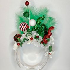 a green and red christmas wreath with ornaments on it's headband, sitting against a white wall