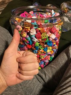 a person is holding their thumb up in front of a glass container filled with toys