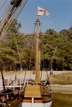 an old sailing ship docked at a dock with a flag on it's mast