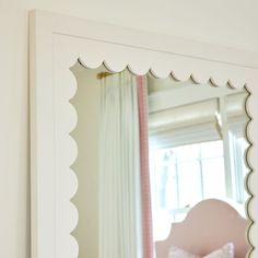 a mirror that is on the side of a wall next to a pink chair and window