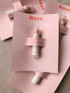 three rose lip balm bottles sitting on top of pink paper with the words, rose lip balm