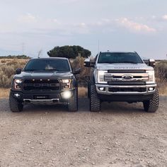 two trucks parked side by side in the dirt