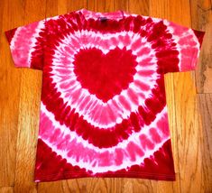 a red and white tie - dye shirt with a heart on the front, sitting on a wooden floor