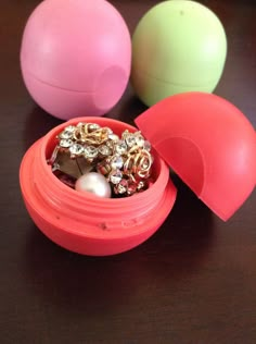 three plastic containers with jewelry in them sitting on a table next to some balls and beads