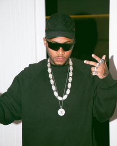 a man wearing sunglasses and a necklace making the peace sign with his hands while standing in front of a door