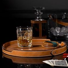 a leather tray with a glass on it next to some glasses and other items in the background