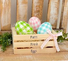 three decorated eggs in a wooden crate with the words farm fresh on it and an egg laying next to each other