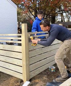 two men are working on a wooden fence