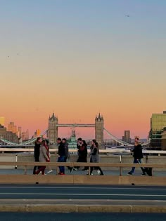 people walking across a bridge in front of the london skyline at sunset, with tower bridge in the background