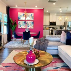 a living room filled with furniture next to a kitchen and dining room table in front of a pink wall