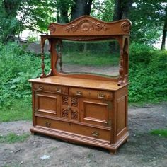 an old wooden dresser sitting in the middle of a field with grass and trees behind it