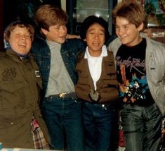 four young men standing next to each other in front of a table with a cake on it