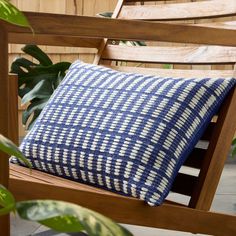 a blue and white pillow sitting on top of a wooden bench next to a plant