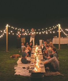 a group of people sitting at a long table with lights strung over it and onlookers