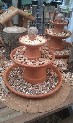 three clay pots filled with rocks and gravel on top of a wooden table covered in wood chips