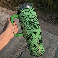 a hand holding a green coffee cup with spider webs on the outside and inside