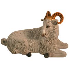 a ceramic goat laying down with horns on it's head and tail, looking to its left