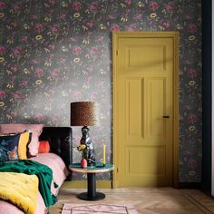 a bedroom with floral wallpaper and pink bed in the corner, next to a yellow door