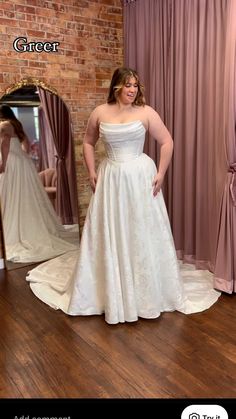 a woman standing in front of a mirror wearing a white wedding dress and posing for the camera