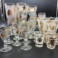 a collection of glass goblets and glasses on a black table with gold leaf designs