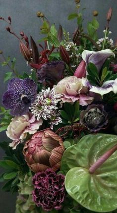 a vase filled with lots of different colored flowers and greenery on top of a table