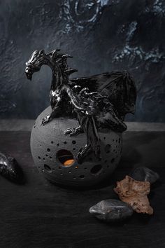 a black dragon statue sitting on top of a gray vase next to rocks and leaves