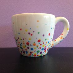 a white coffee cup with multicolored dots on it sitting on a black table