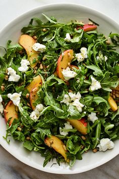 a white bowl filled with green salad topped with peaches and feta cheese on top