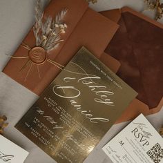 the wedding stationery is laid out on top of each other, including an orange envelope and gold foil