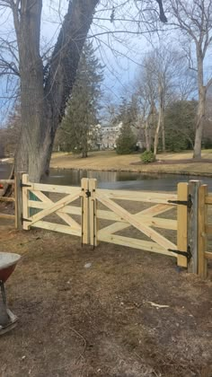 a wooden gate is open in front of a pond and tree with no leaves on it