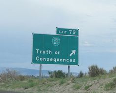 a green exit sign sitting on the side of a road next to a lush green field