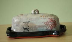 a ceramic covered dish with a chair design on the front and bottom, sitting on a wooden table