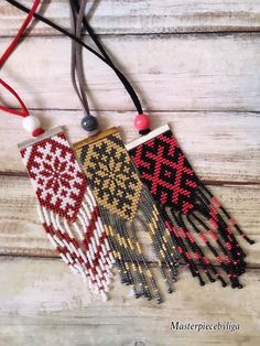 three beaded necklaces are hanging on a wooden surface, one is red and the other is black