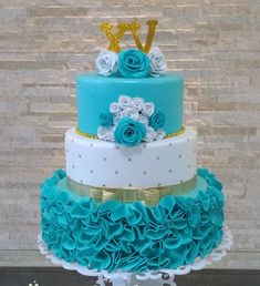 a three tiered cake with blue ruffles and gold letters on top, sitting on a table